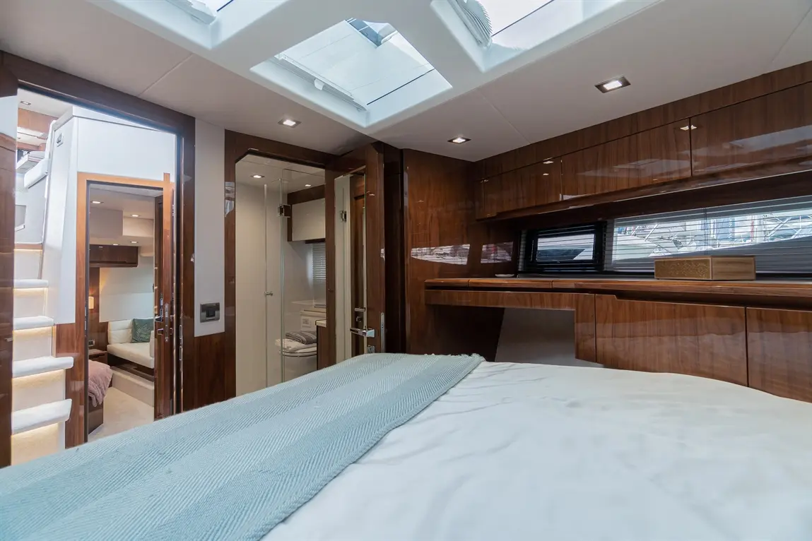 Stylish yacht interior featuring a double bed, wooden cabinetry, and skylights, with access to a lounge area and bathroom.